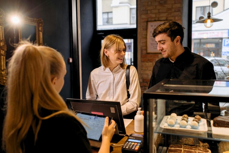 Bezahlvorgang in einer Bäckerei, Kunden stehen an der Kasse zum Bezahlen, Mitarbeiterin an der Kasse