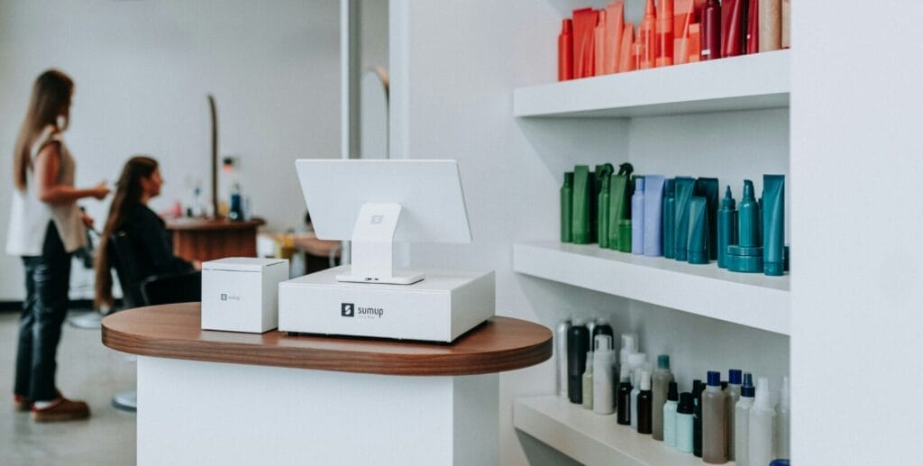Moderne Kasse in einem Friseursalon, Haarpflegeprodukte in den Regalen, Friseurin und Kundin im Hintergrund