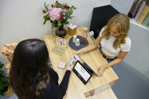 Kundin bezahlt im Kosmetikstudio an einer digitalen Kasse. Auf dem Tisch stehen Blumen und Pflegeprodukte.